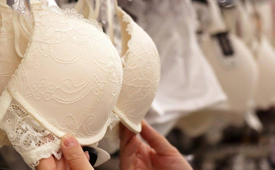 Lingerie store, woman chooses beige lace bra hanging on rack